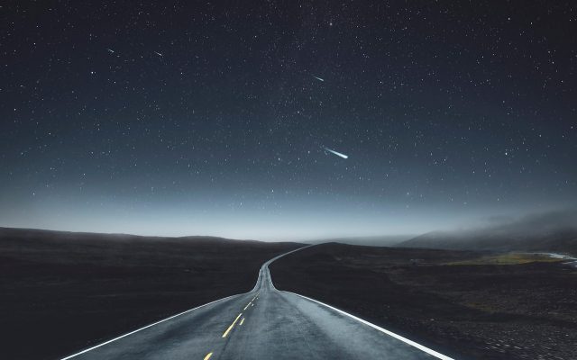 雪山与公路的实景画面，远景中一辆车行驶在空旷道路上，呈现冒险生存剧的开阔冷峻色调